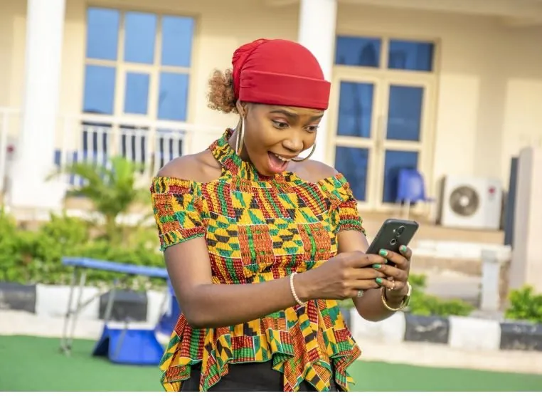 A smiling TAI DT Sacco member checking her account on her phone